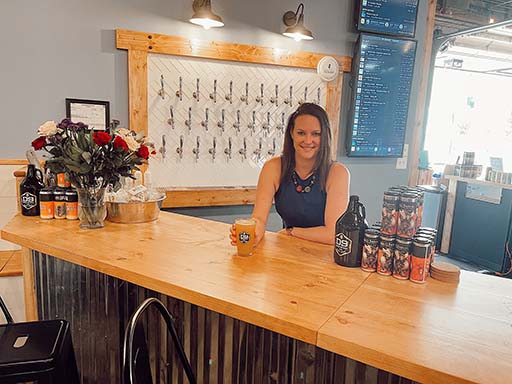Megan Miller of Community Brewing Ventures (CBV), standing behind the bar serving a beer.